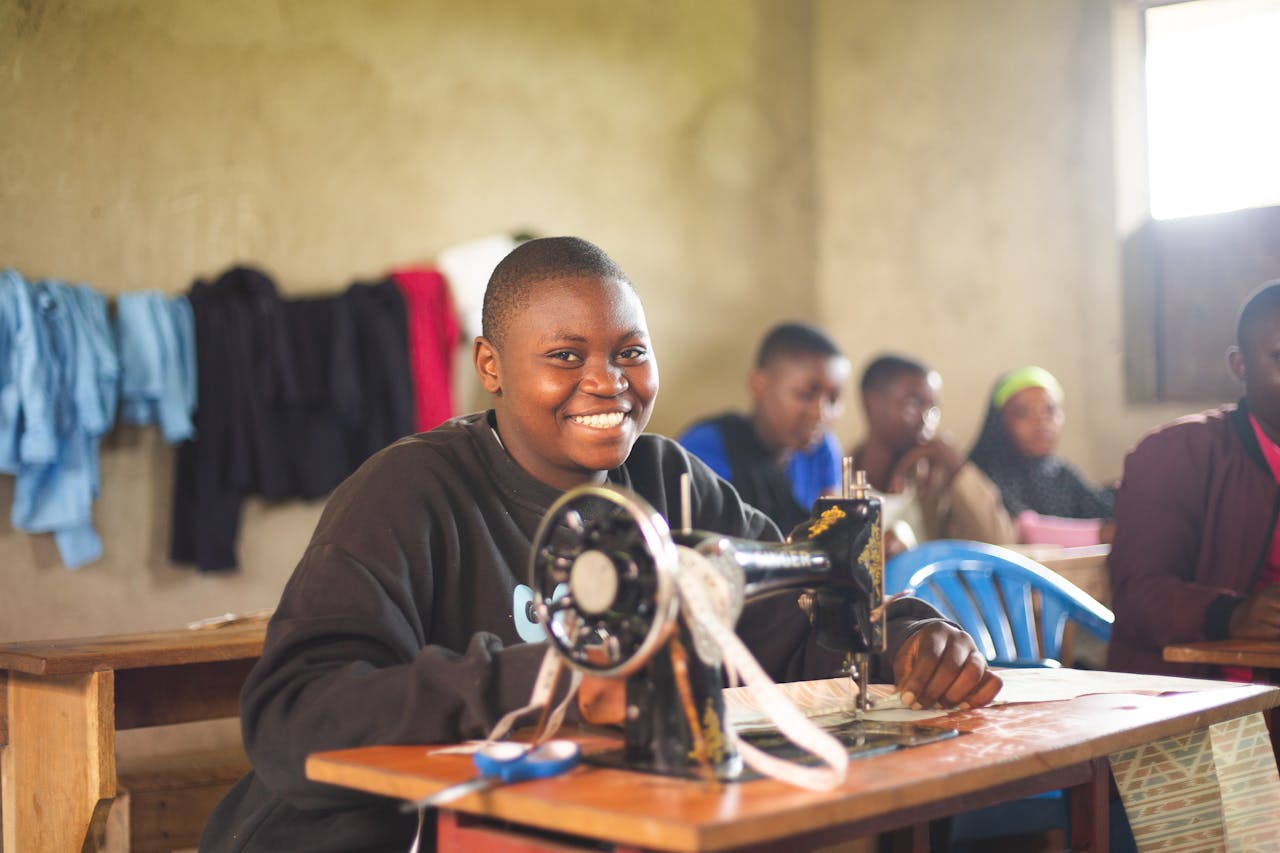 who-we-are Happy student in Uganda using sewing machine in class, highlighting education.